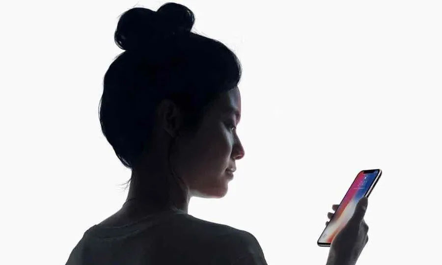 A screenshot of Apple&#x27;s demonstration of FaceID phone unlocking. A woman is looking down at her iPhone